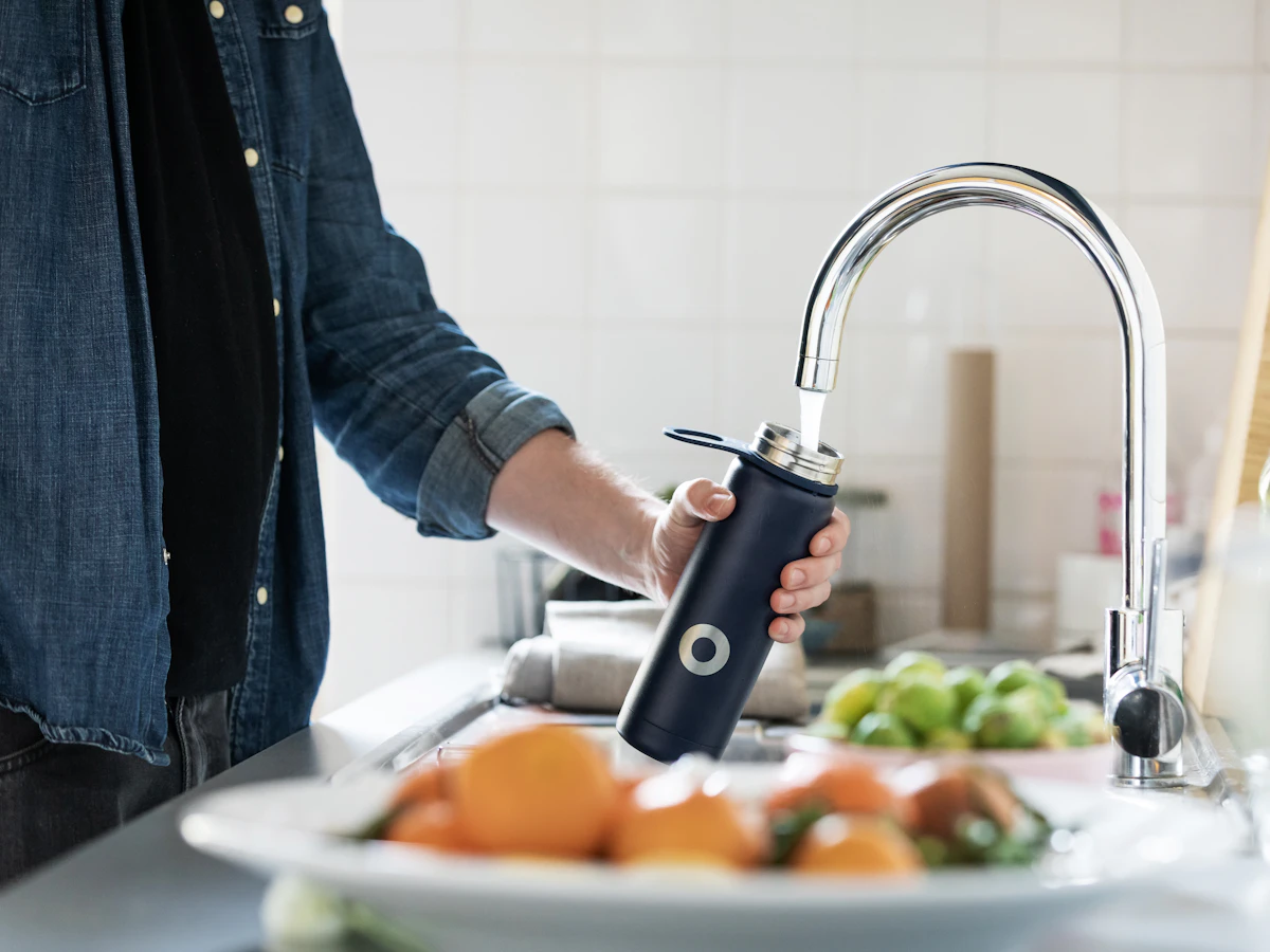 Homeowner filling a reusable bottle at the kitchen faucet after a whole-home filtration install