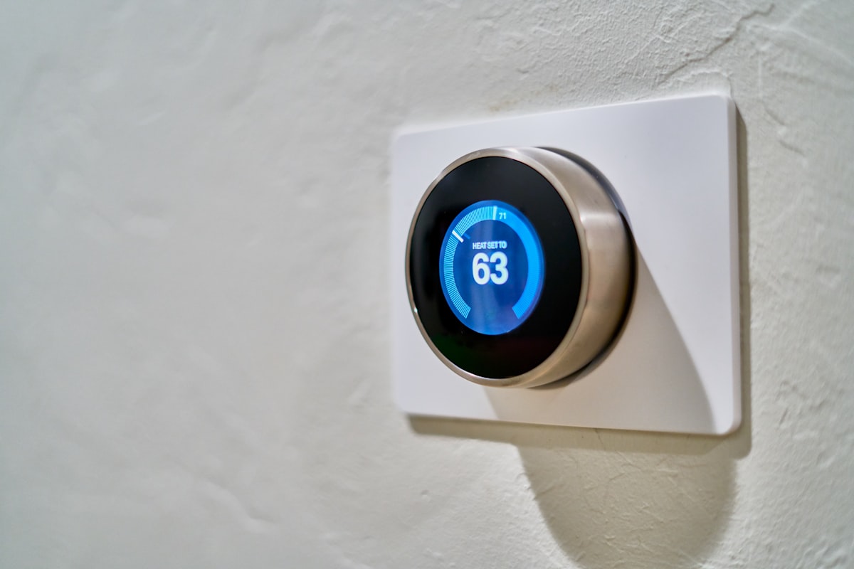 A smart thermostat set to heat glowing blue on a hallway wall while the furnace blows cold air