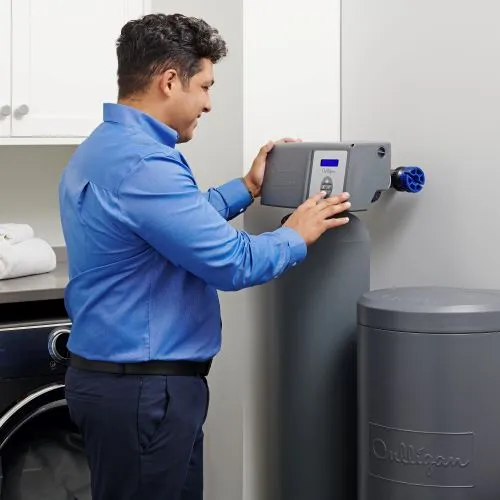 Technician adjusting the control valve on a whole-home water softener and brine tank in an Ohio utility room