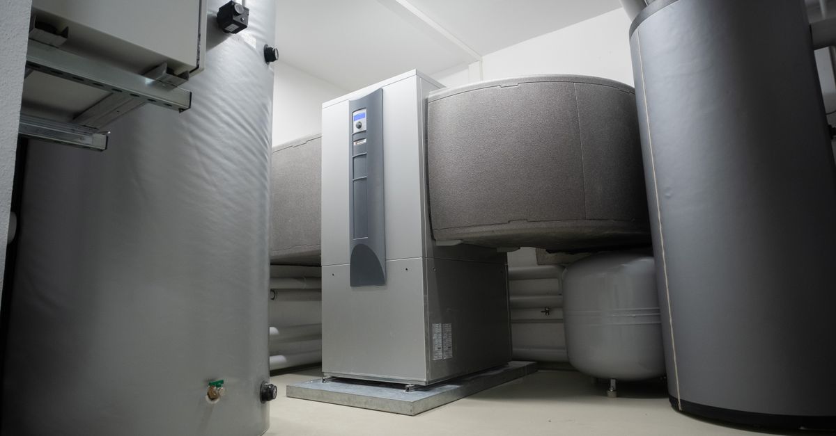 Floor-standing indoor heat pump unit on a steel base plate, flanked by insulated buffer tanks in a home mechanical room